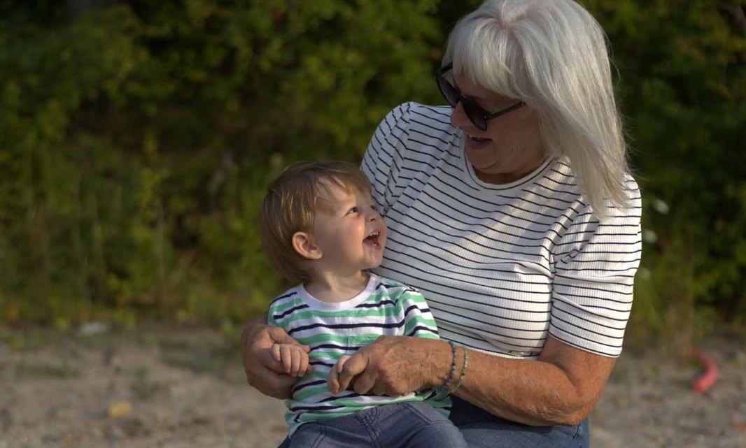 A woman and a toddler sitting together on a driftwood log at the beach.
