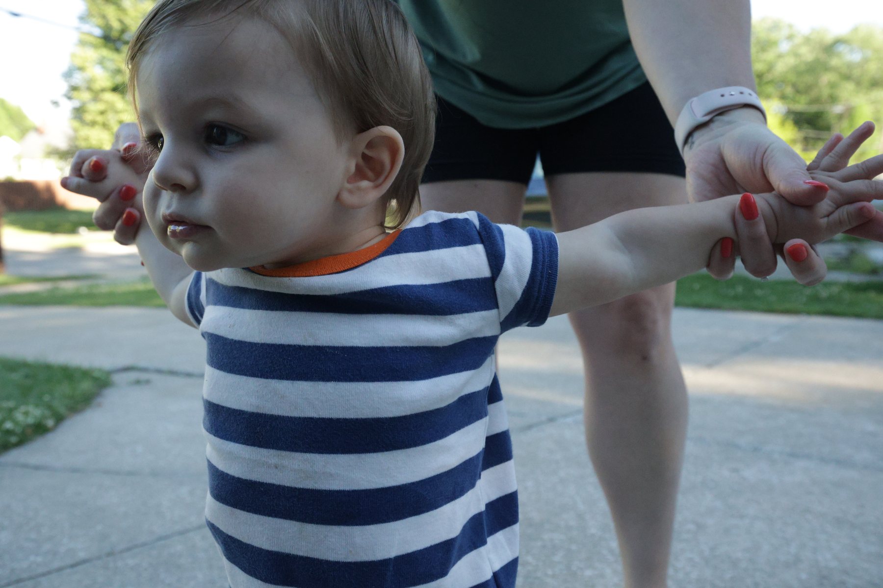 Toddler holding a parent's hands on a walk.