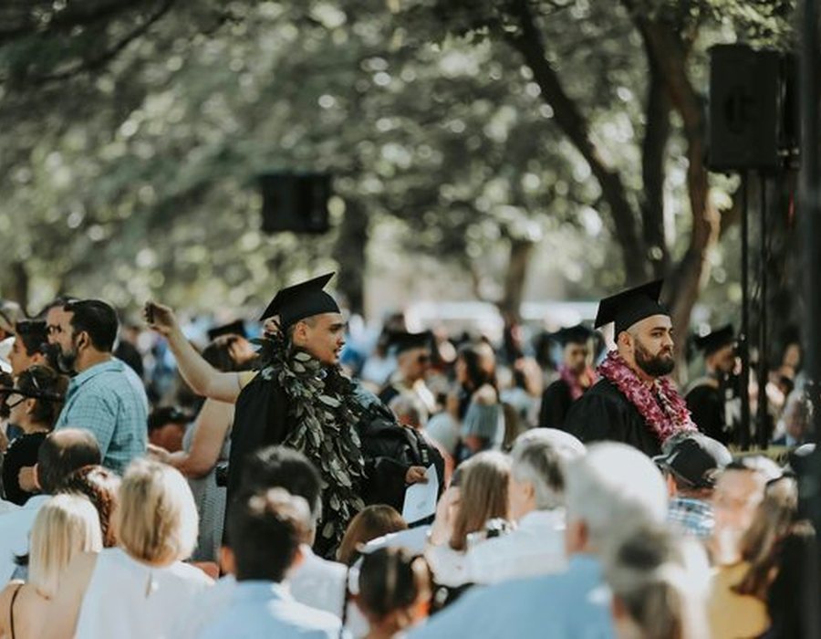 Graduates in caps and gowns among family and guests at a commencement ceremony.